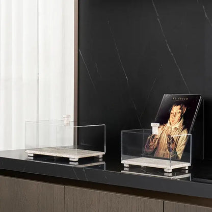 Modern acrylic display case with travertine base holds art books on black countertop for dining room use