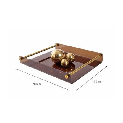 A sleek amber acrylic fruit plate tray with polished brass handles holding three gold spheres on a reflective surface