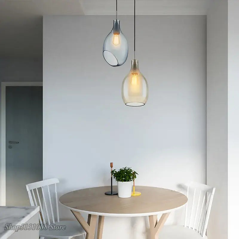Two modern glass pendant lights in translucent blue and warm amber hues hang above a kitchen dining table