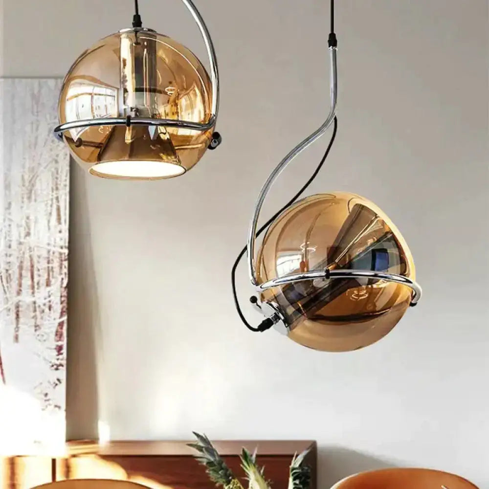 Two modern pendant lights with spherical amber glass pendant shades and chrome metal frames for kitchen use