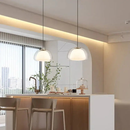 Two modern amber and gray glass pendant lights with frosted shades hang above a kitchen island with thin black cords