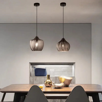 Two sleek dark-toned amber gray glass pendant lights with woven mesh shades hang above a wooden dining table decorbites amber gray