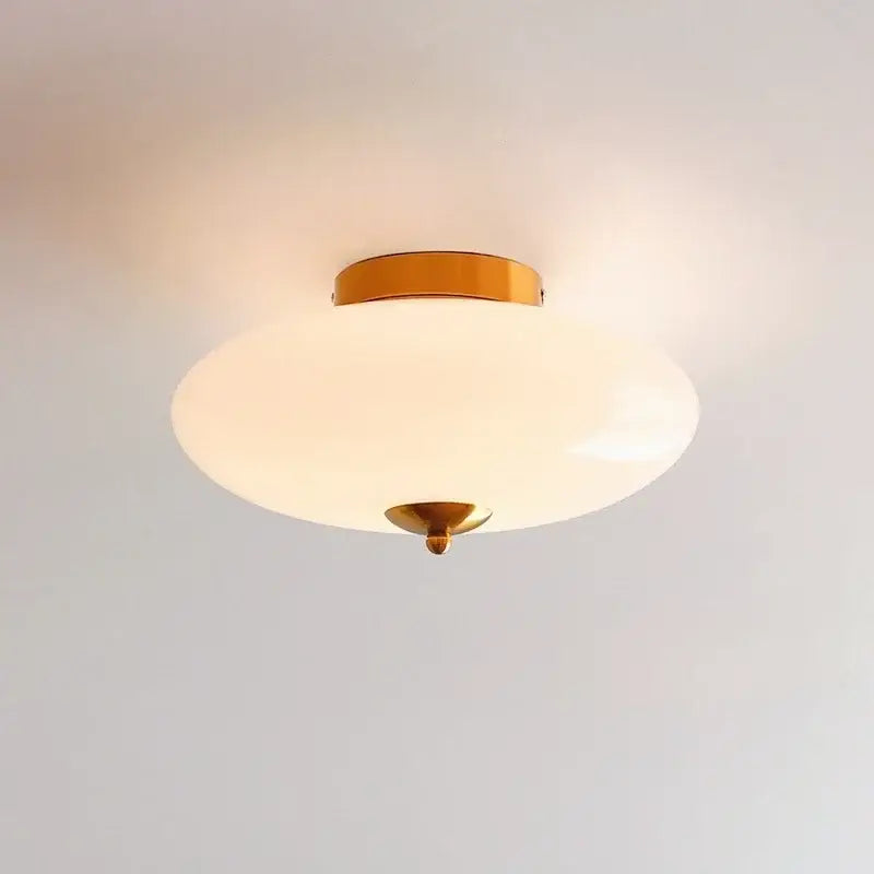 A sleek modern bauhaus cream white ceiling lamp with brass finish and cream white glass shade for bedroom lighting