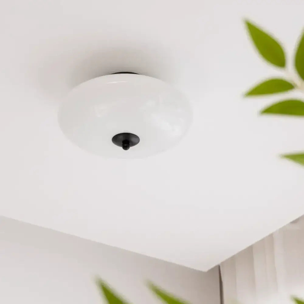 A sleek bauhaus cream white glass ceiling lamp with white frosted glass and black central fixture for bedroom use