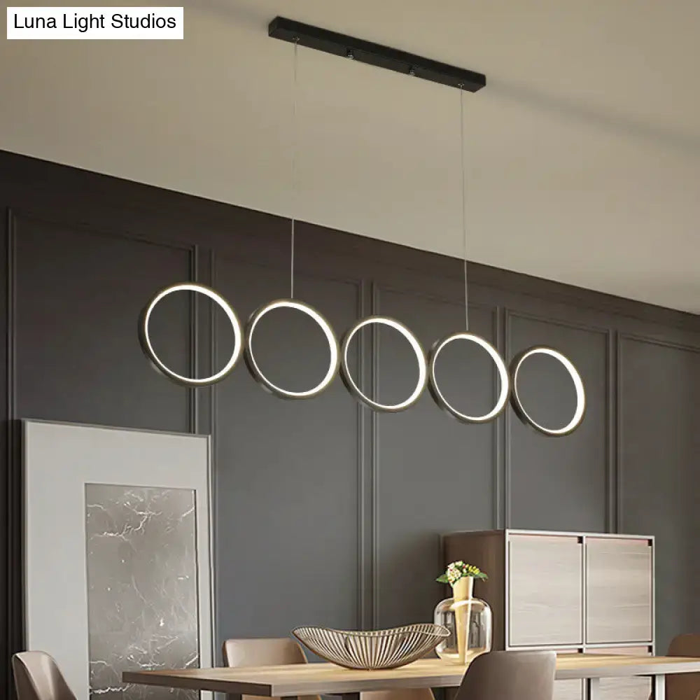 Modern black metal pendant light featuring five glowing circular led rings in a hanging island light design over table