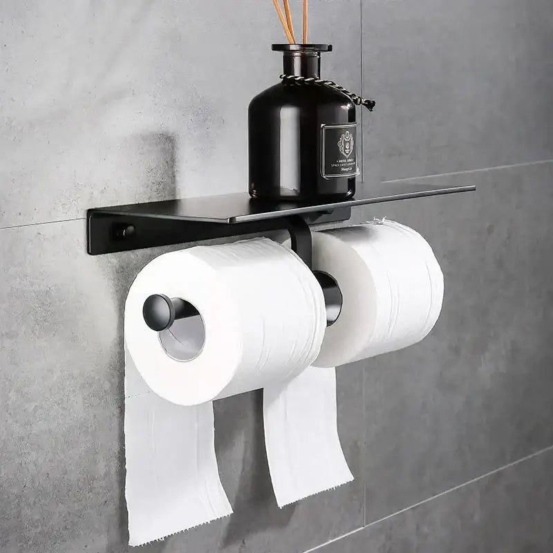 Modern black aluminum wall-mounted toilet paper holder with shelf holding two rolls of white toilet paper