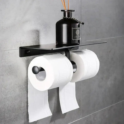 Modern black aluminum wall-mounted toilet paper holder with shelf holding two rolls of white toilet paper