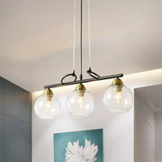 Modern black metal pendant light with three smoke gray glass globes and brass accents for dining hall island