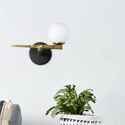 Modern black and brass wall sconce with a matte base and white glass ball shade for bedroom lighting