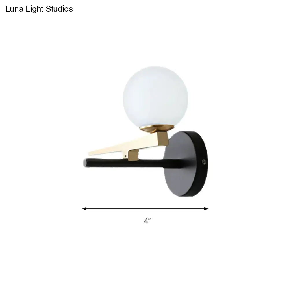 Modern black and brass wall sconce with a frosted white glass ball shade for bedroom lighting
