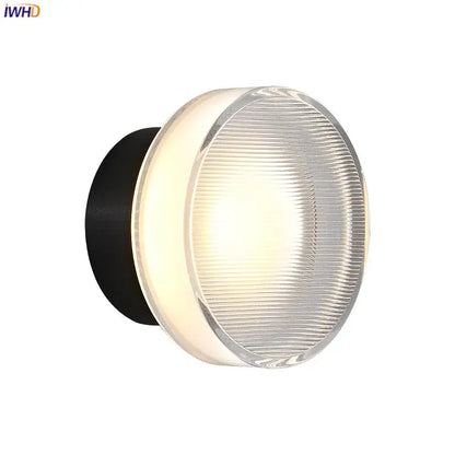 Modern black and clear acrylic wall sconce light with round ribbed glass diffuser emitting warm light for bedroom use