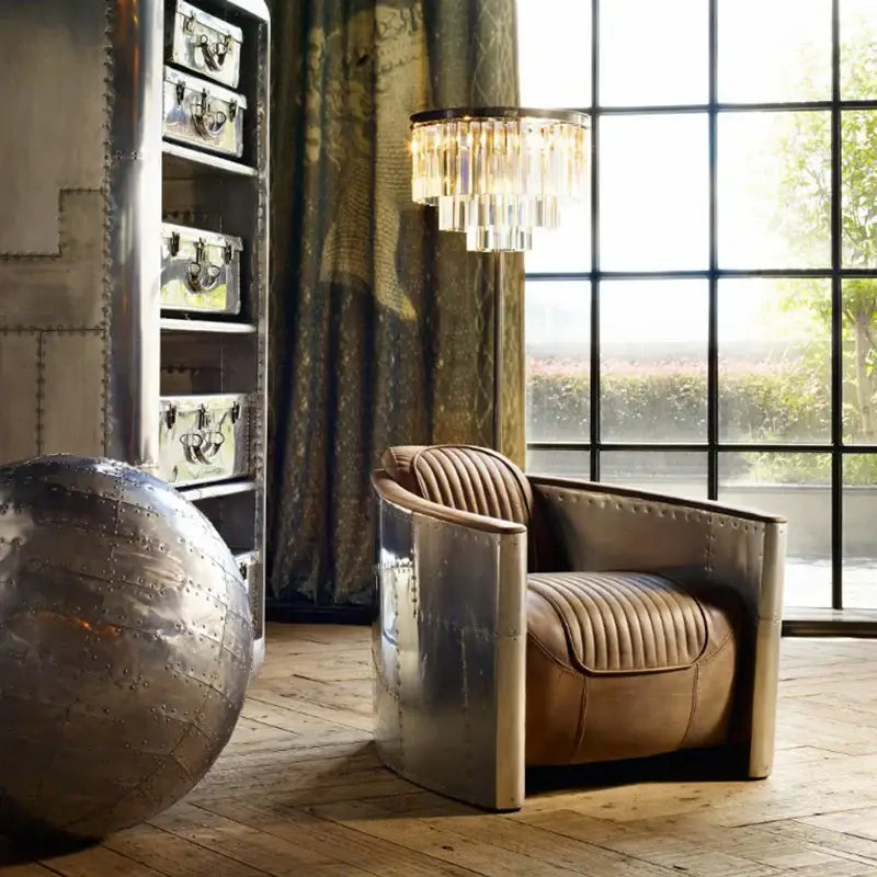 A sleek vintage-inspired armchair with metallic silver frame and tan leather upholstery next to a modern black and gold crystal floor lamp
