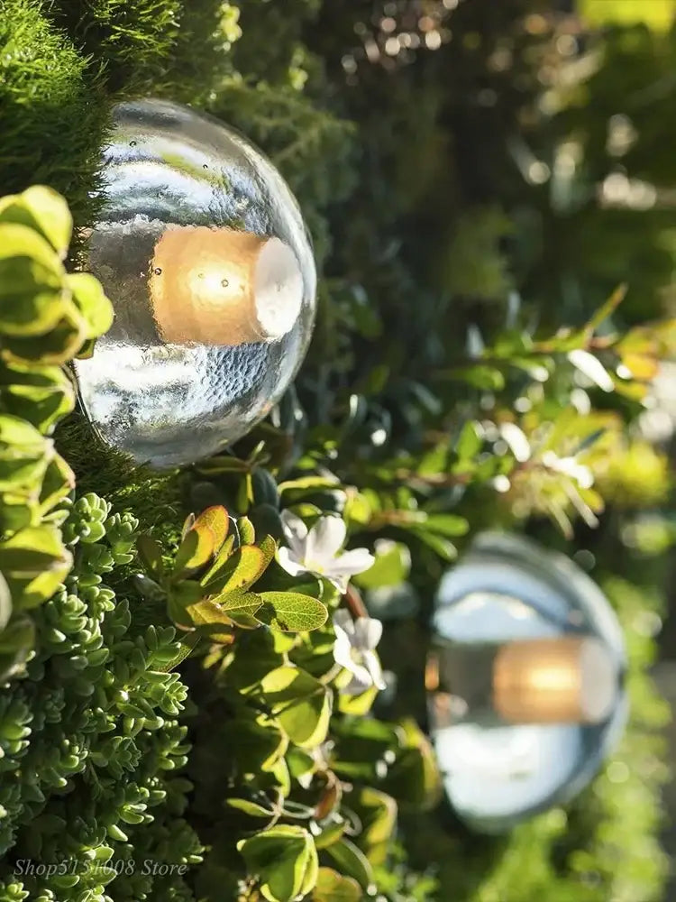 Modern black and gold crystal wall light with a clear textured glass sphere surrounded by green foliage for outdoor decorbites crystal wall use
