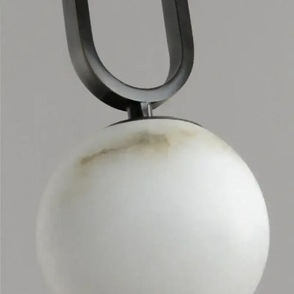 A sleek matte black u-shaped metal pendant light suspends a white marble orb with a polished copper finish shade