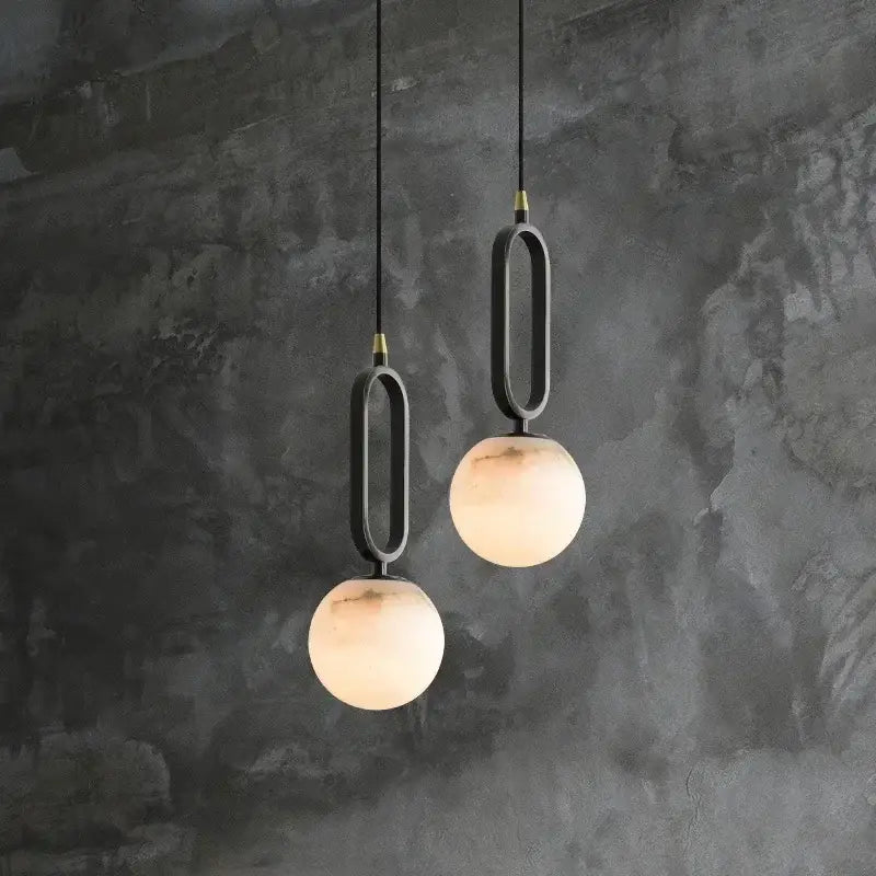 Modern pendant lights with matte black frames and warm frosted glass spheres featuring polished copper finish accents
