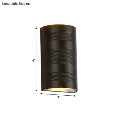 Dark bronze cylindrical outdoor wall lamp with horizontal ribbed texture and warm white light from the bottom