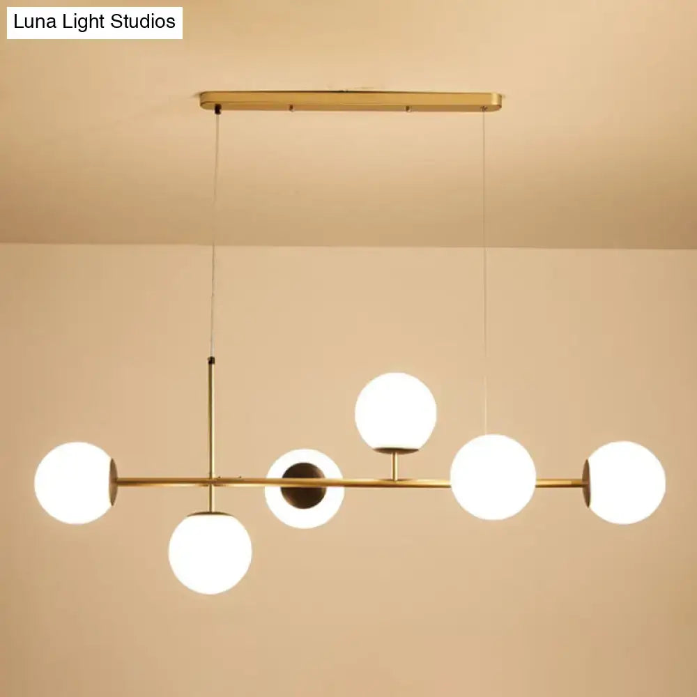 Modern black and white bird linear island pendant light with brass frame and five frosted glass globe shades in asymmetrical design