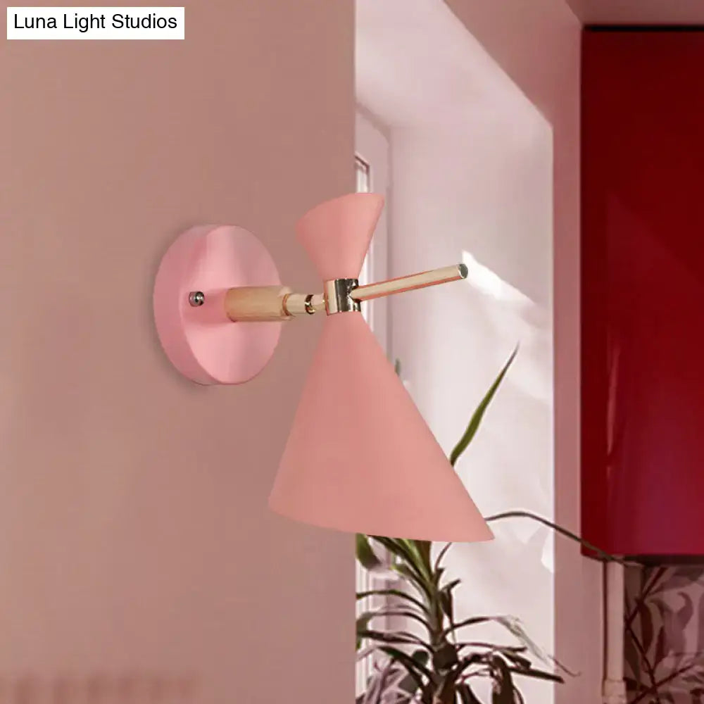 Pastel pink conical wall sconce with wooden arm and brass hardware featuring a modern black angle shade design