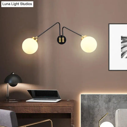 Modern black and brass wall lamp with double-arm design and milk glass spherical shades for bedroom sconce use