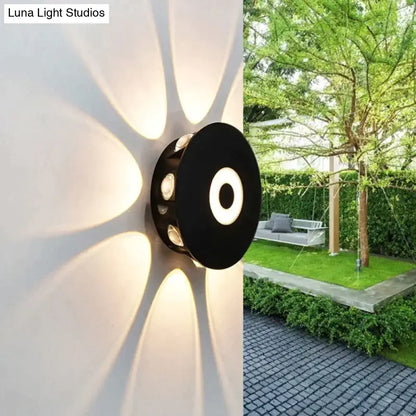 Modern black circular led outdoor wall sconce with multiple embedded lights casting warm radial glow on outdoor wall