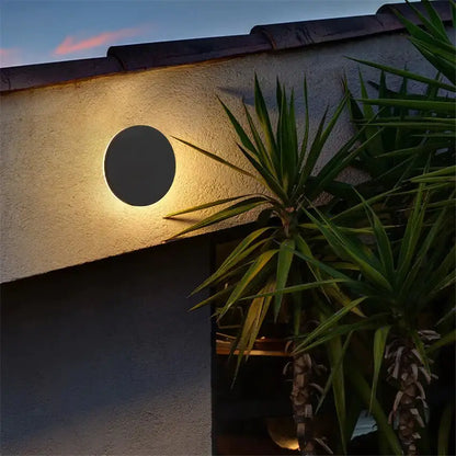 Modern black circular waterproof wall lamp emitting warm glow on textured stucco exterior in bedroom setting
