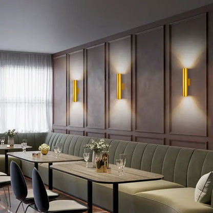 Three gold-finished cylindrical decorbites cob led wall lamps illuminate dark wood walls in modern minimalist style