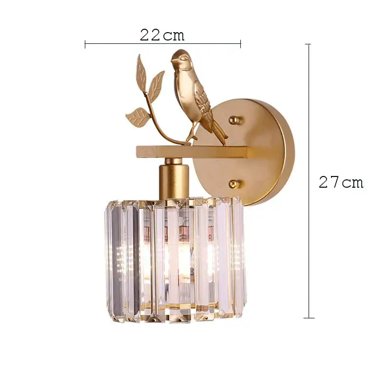 Gold-toned wall lamp decorbites crystal bird featuring a bird on a branch above a cylindrical crystal shade for bedroom decor