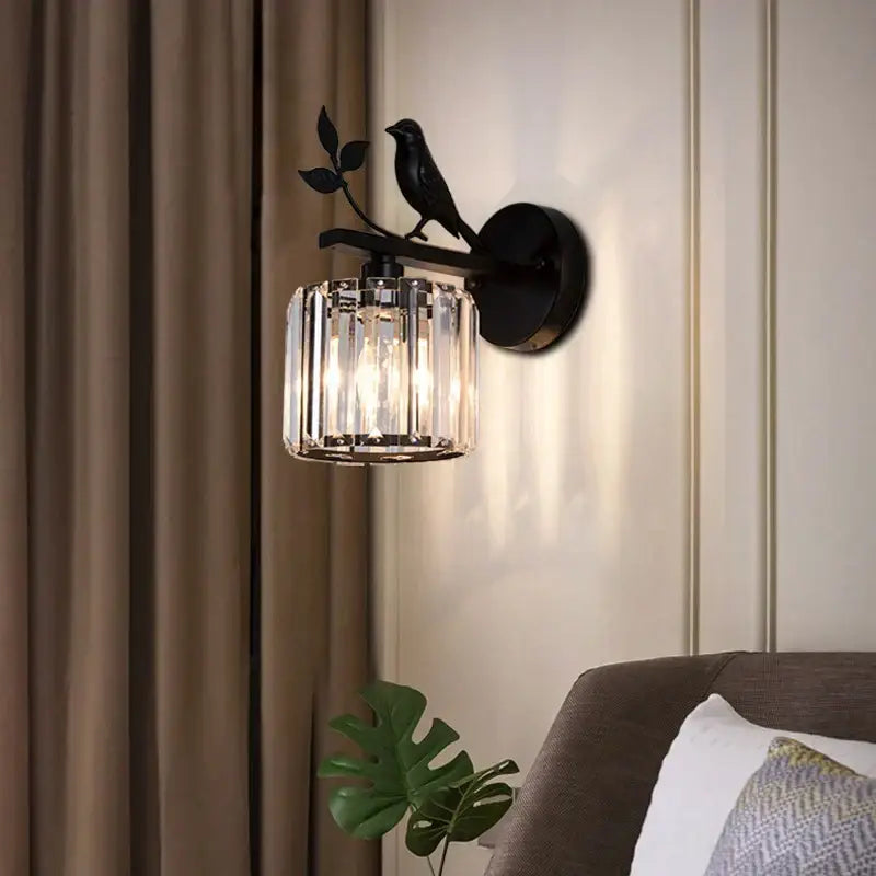 Modern black crystal bird wall lamp featuring a wrought iron sconce with a perched bird and cylindrical crystal shade