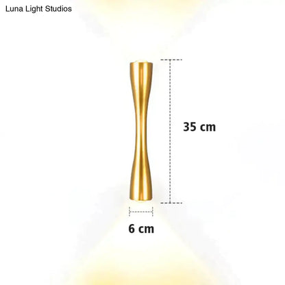 A sleek gold-toned metal wall sconce 35 cm tall with slender hourglass design for modern black curved outdoor porch lighting