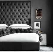 Modern black glass and metal semi oval wall light with black finish mounted above a black tufted leather headboard with diamond pattern stitching