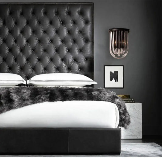 Modern black glass and metal semi oval wall light with black finish mounted above a black tufted leather headboard with diamond pattern stitching