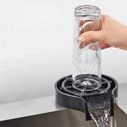 Clear glass tumbler being rinsed by hand over modern black glass rinser sink with plastic bar drain for cup washing