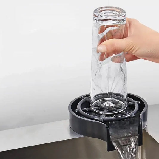 Clear glass tumbler being rinsed by hand over modern black glass rinser sink with plastic bar drain for cup washing