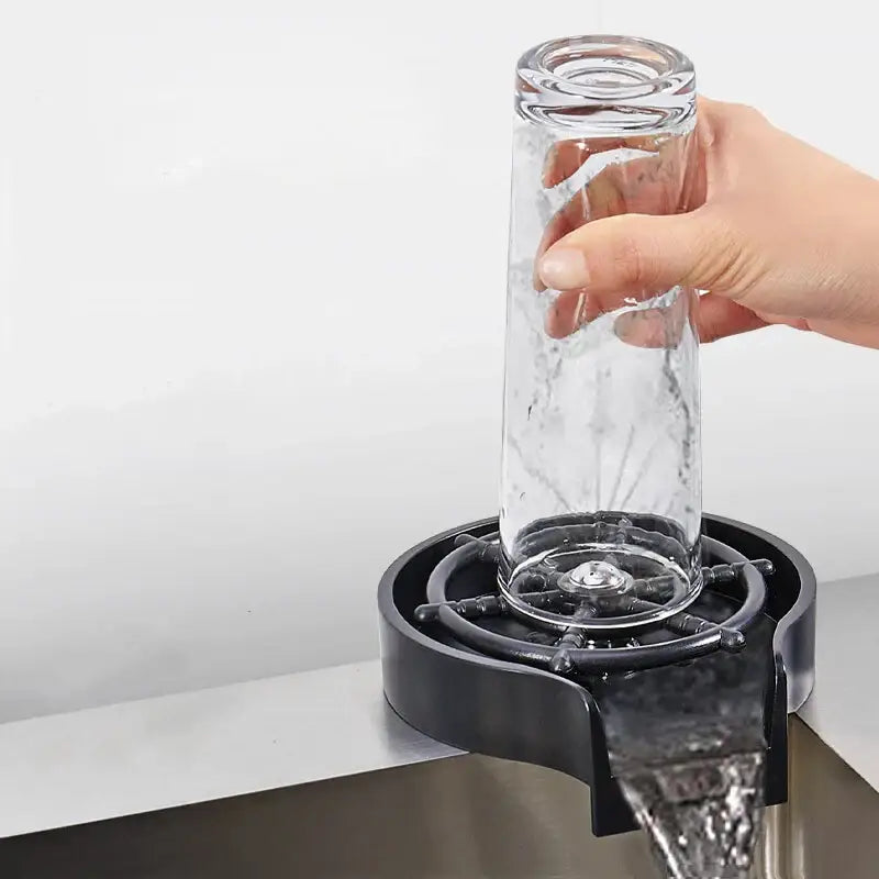 Clear glass tumbler being rinsed by hand over modern black glass rinser sink with plastic bar drain for cup washing