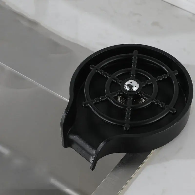 Modern black glass rinser sink with a black plastic coffee cup holder featuring a ship’s wheel design and metallic center
