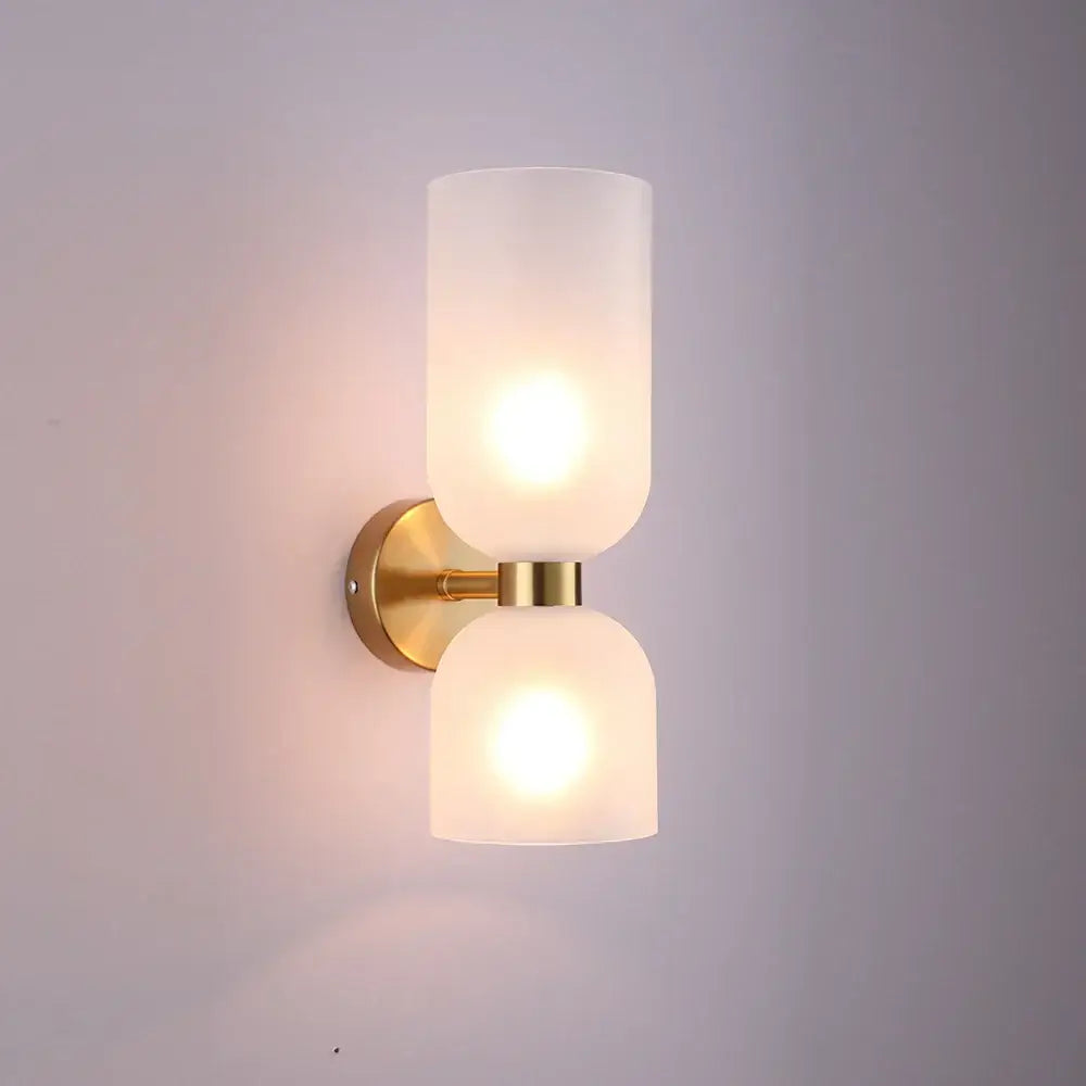 Gold-toned wall lamp with two frosted glass shades emitting warm glow in modern black glass shade wall design