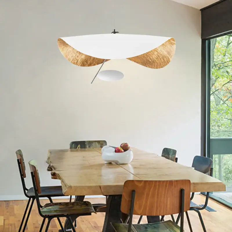 Modern black and gold abstract lederam manta pendant light with white curved glass shade and gold-leafed wooden accents above dining table