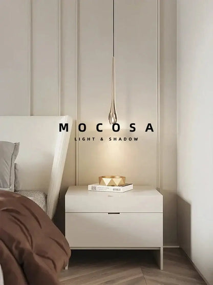 A modern black and gold droplet pendant light with metallic finish and remote control hangs above a nightstand