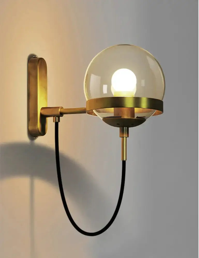 Brass-finished wall sconce lamp with black metal arms and glass globe for modern bedroom lighting sconce lamps
