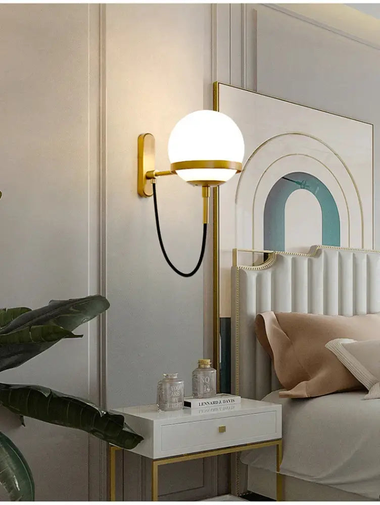 Modern black and gold wall sconce lamp with a spherical white glass globe and slender metallic arm for bedroom lighting