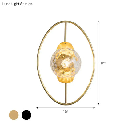 Modern black and gold wall lamp with gold-toned oval metal frame and textured translucent white glass globe fixture