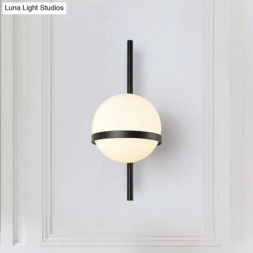 Modern black and gold glass shade wall sconce with a frosted globe and horizontal accent band for bedroom light