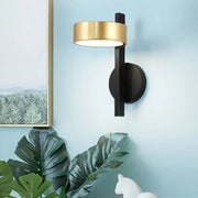 Modern wall lamp with a sleek black base and gold-finished circular head designed as a bedroom reading light