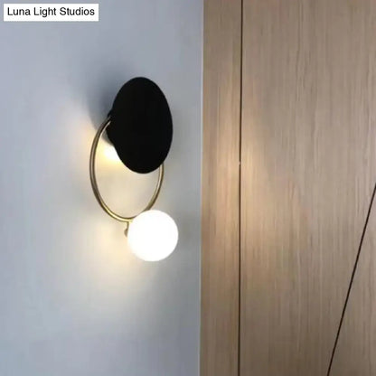 Modern black and gold metal planet wall mount lamp with circular shade and glowing white spherical bulb for bedroom sconce