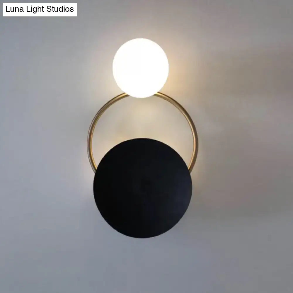 Modern black and gold metal planet wall mount lamp with glowing white spherical bulb and matte black disc frame sconce