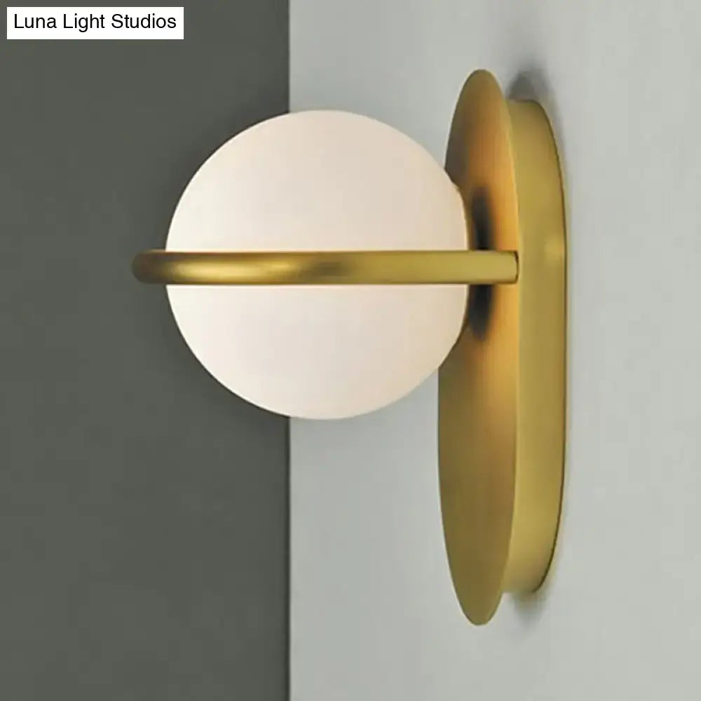 Gold-toned wall light with milk glass frosted spherical shade and black metal backplate for modern bedroom use