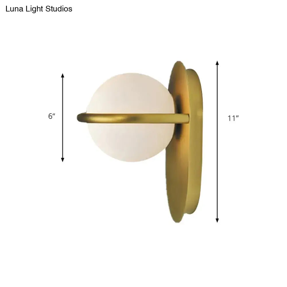 A modern black and gold wall light with milk glass globe and sleek metal backplate for bedroom lighting