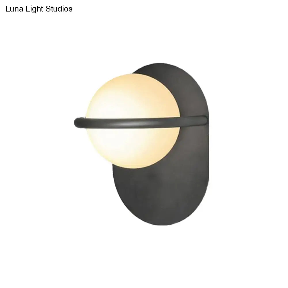 Modern black and gold wall light with warm milk glass shade and metal backplate for bedroom lighting