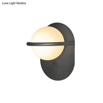Modern black and gold wall light with warm milk glass shade and metal backplate for bedroom lighting