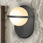 Modern black wall light with warm glowing milk glass shade and metal backplate suitable for bedroom lighting